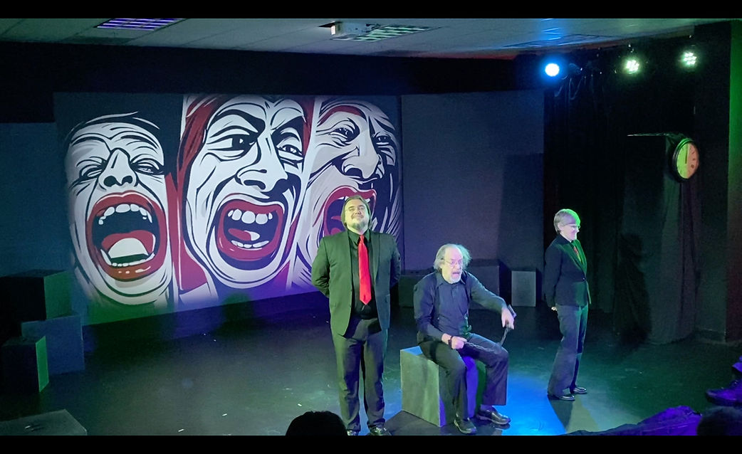 Three TAO performers on a stage lit blue and green, in front of a backdrop of expressive faces.